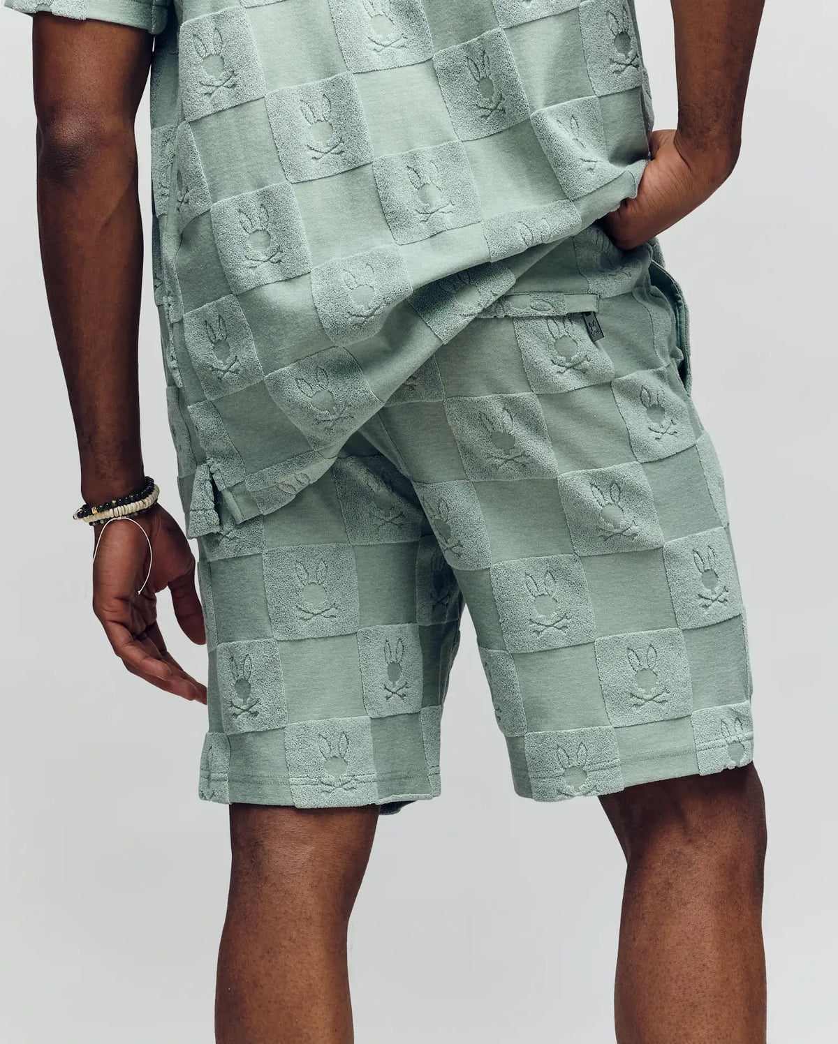 A person shown from the back wearing Psycho Bunny’s MENS KELVIN TOWEL TERRY SWEATSHORT (MB0900006) and matching shirt in light green jacquard terry with a raised Checkered Bunny pattern.