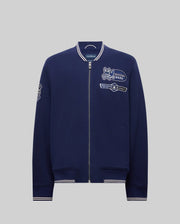 The Psycho Bunny MENS DESMOND PIQUE KNIT BOMBER - MO1100018 is a navy bomber with white trim, varsity-style details, and embroidered patches including a bunny logo, "Psycho Bunny" text on the chest, and a sleeve patch.