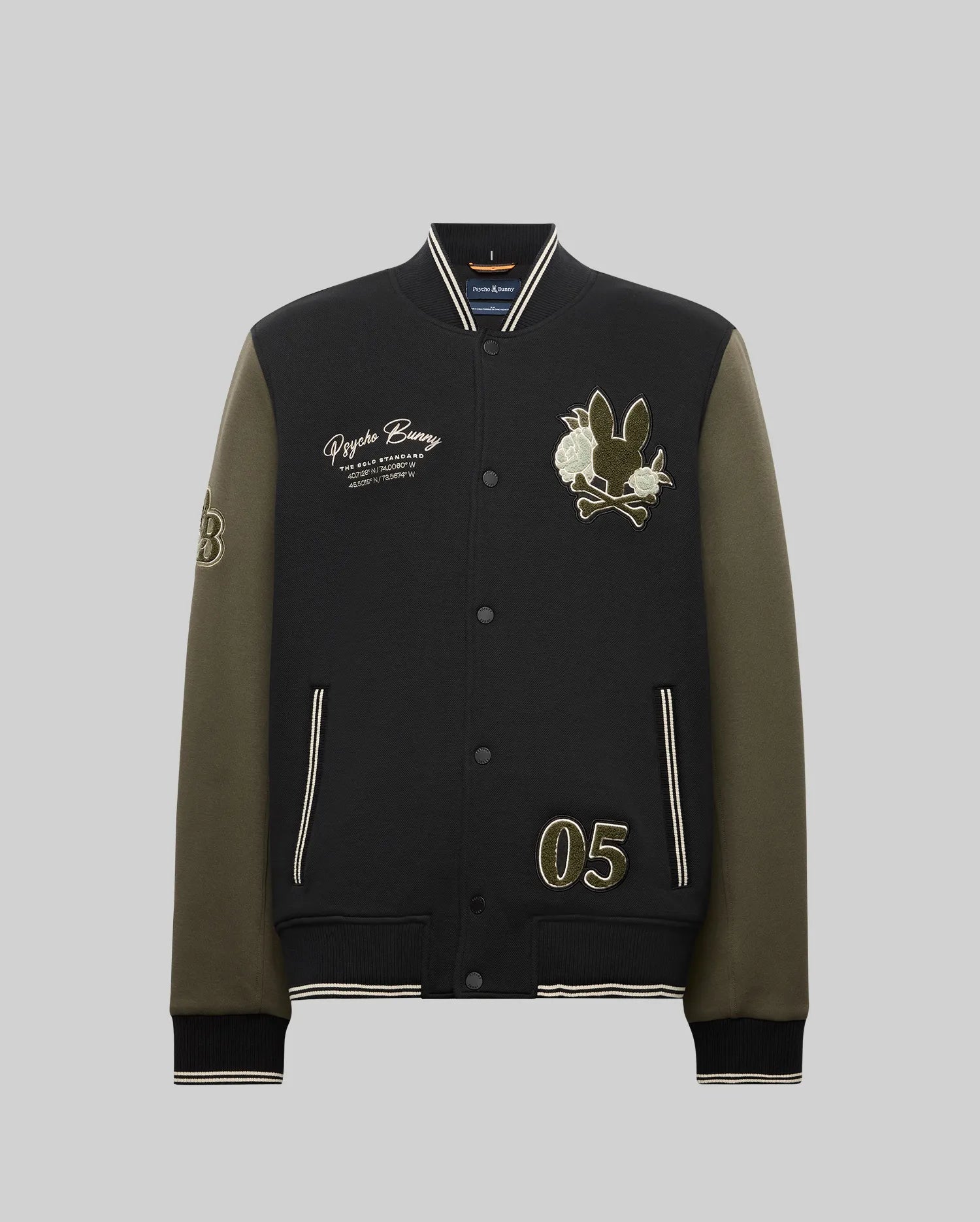 The Psycho Bunny MENS AUGUSTE KNIT BOMBER (MO1100050) is a black and olive varsity jacket with front snap buttons, embroidered text, chenille bunny and flower patches, number "05" on one side, and "53" on the sleeve; shown on a gray background.