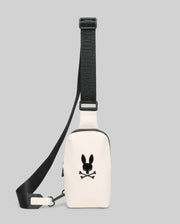 Mens Rubberized Crossbody in cream, featuring a smooth finish, a prominent black Psycho Bunny skull logo on the front, and an adjustable black strap with repeated brand text.