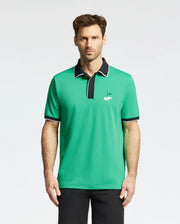 A man stands against a plain white background, showcasing the Psycho Bunny MENS CLAYTON PIQUE POLO - MT0100004. Made from premium Pima cotton, this breathable polo features a small golf hole and flag logo on the chest and has contrasting black collar and sleeve trim.
