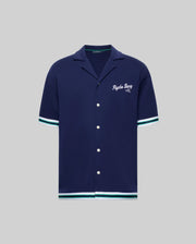 The Psycho Bunny MENS BASIL TAPED CAMP COLLAR SHIRT (MT0500004) is a navy, short-sleeve cotton-modal shirt with white buttons, white and teal striped sleeve/hem trim, and "Psycho Bunny 2005" embroidered on the left chest.