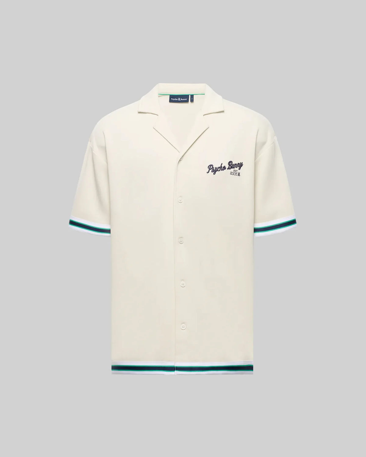 The Psycho Bunny MENS BASIL TAPED CAMP COLLAR SHIRT (MT0500004) is cream-colored, made of a cotton-modal blend with short sleeves, green/blue stripe accents, a Johnny collar, and embroidered "Psycho Bunny" text on the left chest.