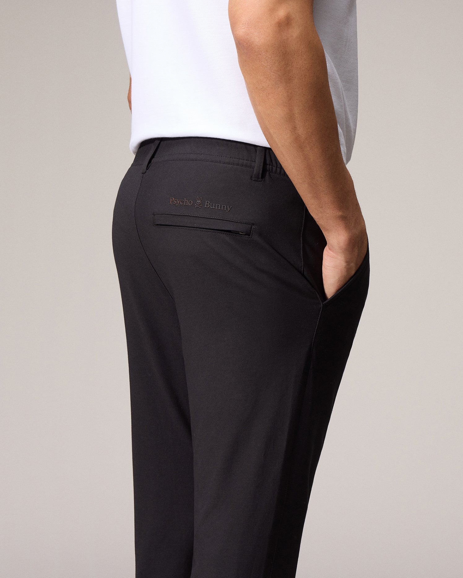 Back view of a person wearing black Psycho Bunny MENS MADISON COMMUTER PANT - B6P395Z1WB with an embroidered Bunny logo on the rear pocket.