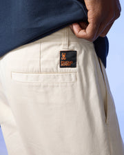 A close-up of a person's hand tucked into the back pocket of beige Psycho Bunny Men's York Chino shorts, featuring a black label with a yellow bunny logo and the text "psycho bunny.