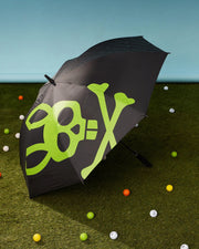 A GOLF UMBRELLA - B6A624C200 by Psycho Bunny, featuring a green skull and crossbones design on a black canopy, stands open on a grass surface. Surrounding this reliable umbrella are variously colored golf balls scattered around. The background is a gradient of light blue, highlighting its excellent rain protection abilities.