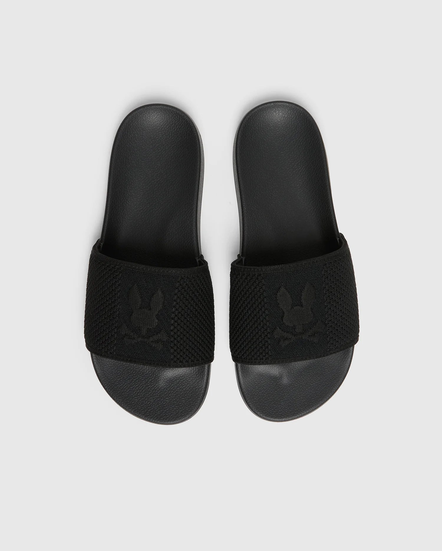A pair of Psycho Bunny's KIDS KNIT SLIDES (B0A377F200) in black with molded footbeds and textured straps featuring a subtle pattern lies side by side on a white background.