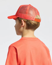 A child in a Psycho Bunny KIDS MELBOURNE GRAPHIC TRUCKER HAT (B0A548F200) featuring an orange hue, snap-back strap, and embroidered icon looks to the side against a plain, light-colored background.