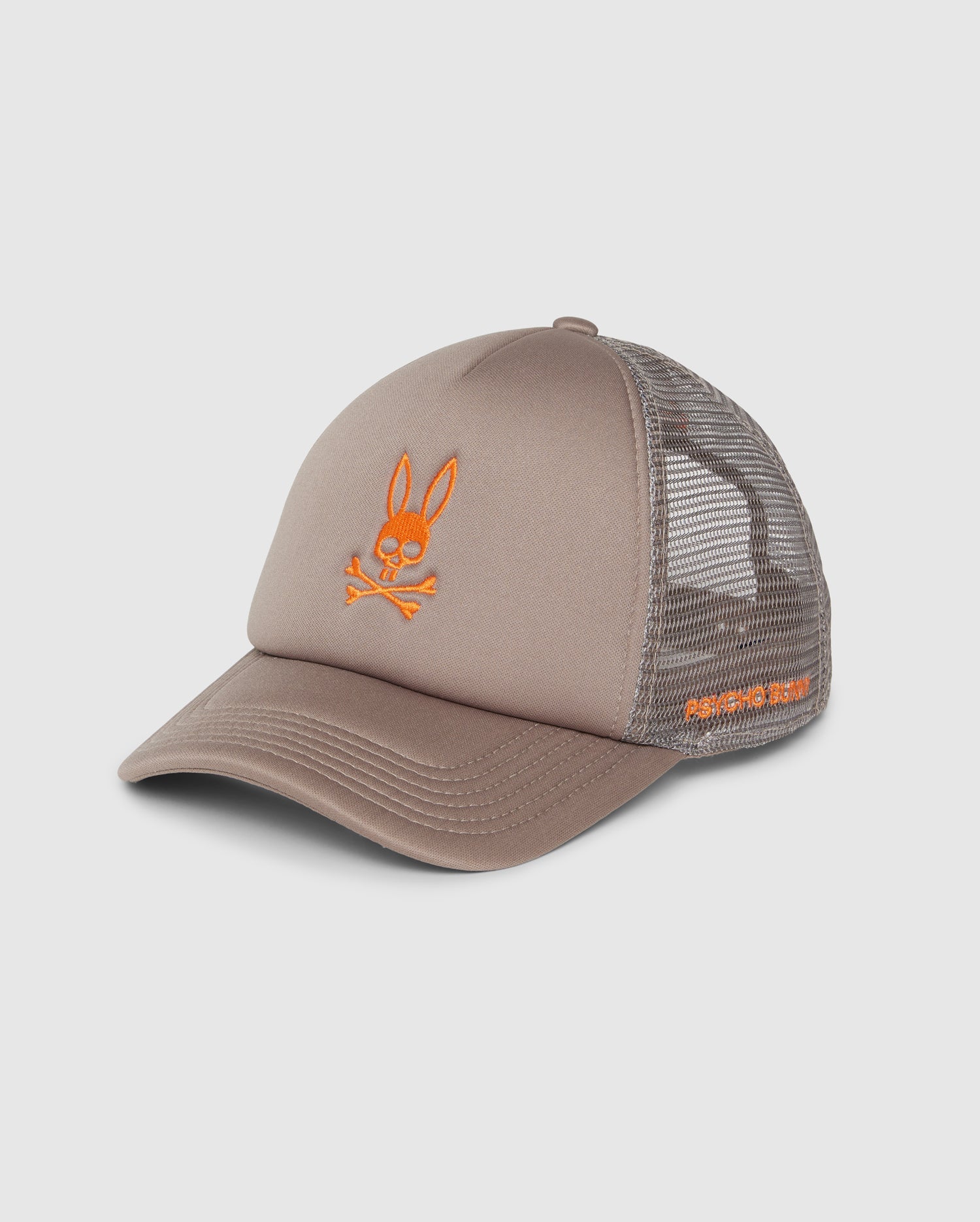 The KIDS PARIS TRUCKER CAP (B0A591C200) by Psycho Bunny features a beige hue with a mesh back and an orange Bunny logo of a rabbit's head above crossbones. The brim has visible stitching, and the side is embroidered with text. This cap blends playful design with trendy flair.