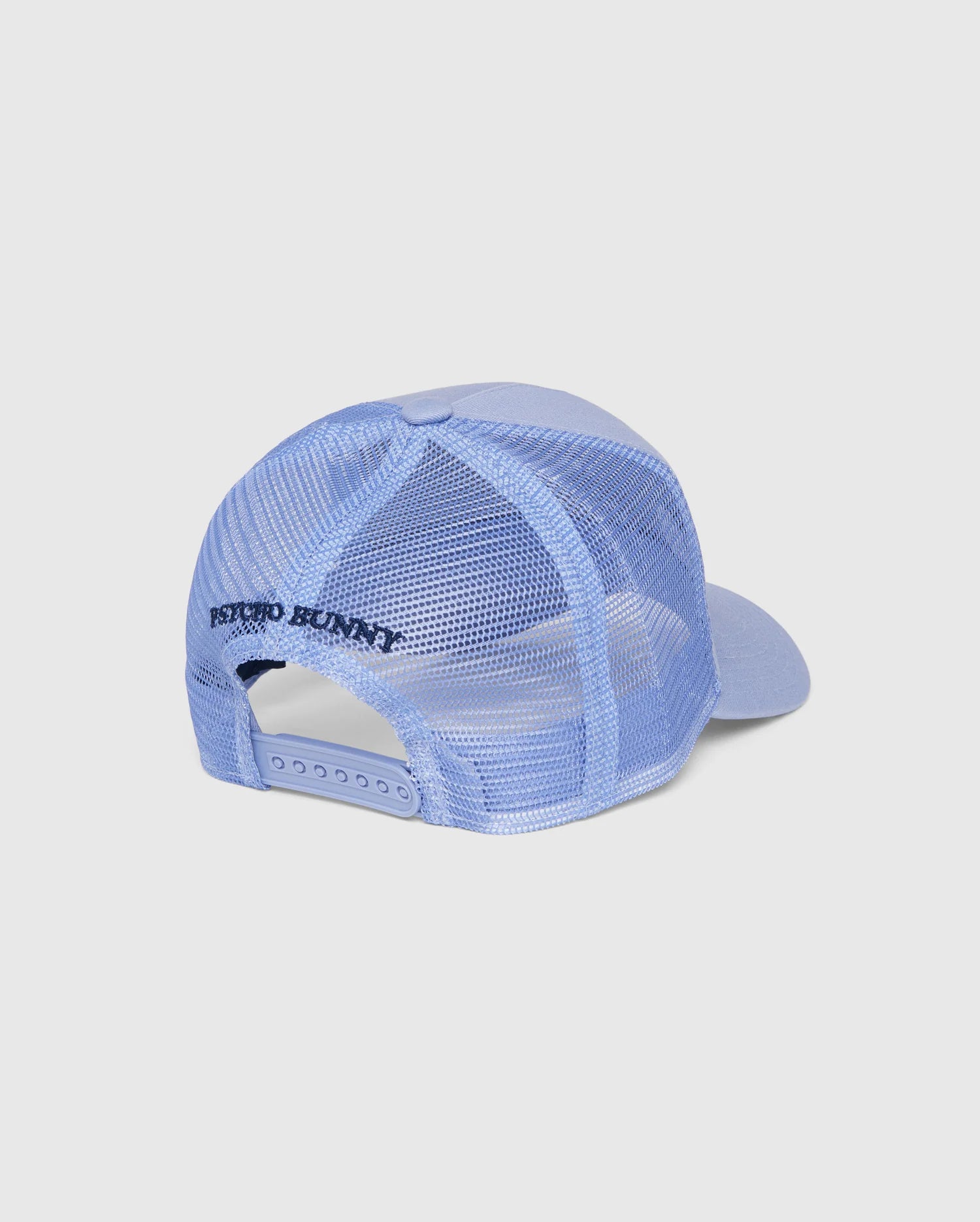 The KIDS RIVIERA TRUCKER CAP - B0A667C200 is a light blue cap with a mesh back and curved brim, capturing the nostalgia of the 2000s. Above the adjustable snapback fastening on the back, "Psycho Bunny" is prominently displayed in black lettering. This trendy cap is showcased against a plain white background.