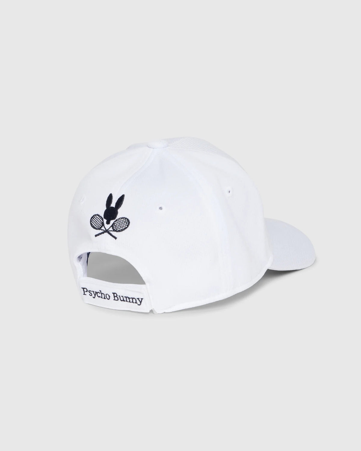 The KIDS COURTSIDE SPORT CAP - B0A685C200 by Psycho Bunny is a white baseball cap for kids, featuring an embroidered bunny with crossed tennis rackets. "Psycho Bunny" is printed on the back strap, making it a classic accessory staple for young athletes.