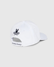 The KIDS COURTSIDE SPORT CAP - B0A685C200 by Psycho Bunny is a white baseball cap for kids, featuring an embroidered bunny with crossed tennis rackets. "Psycho Bunny" is printed on the back strap, making it a classic accessory staple for young athletes.