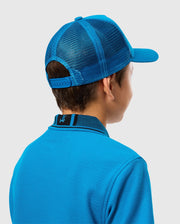 A person wearing a Psycho Bunny KIDS MALTON TRUCKER CAP - B0A797D200 with mesh ventilation and a blue collared shirt is shown from behind. The cap has an adjustable strap, and the shirt features a small emblem on the collar. The background is plain and light-colored.