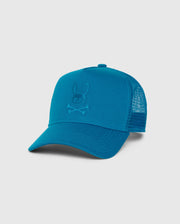 This is the KIDS MALTON TRUCKER CAP - B0A797D200 by Psycho Bunny, a teal blue trucker cap with a curved brim and mesh ventilation at the back. The front panel boasts an embroidered logo of a skull and crossbones with bunny ears.