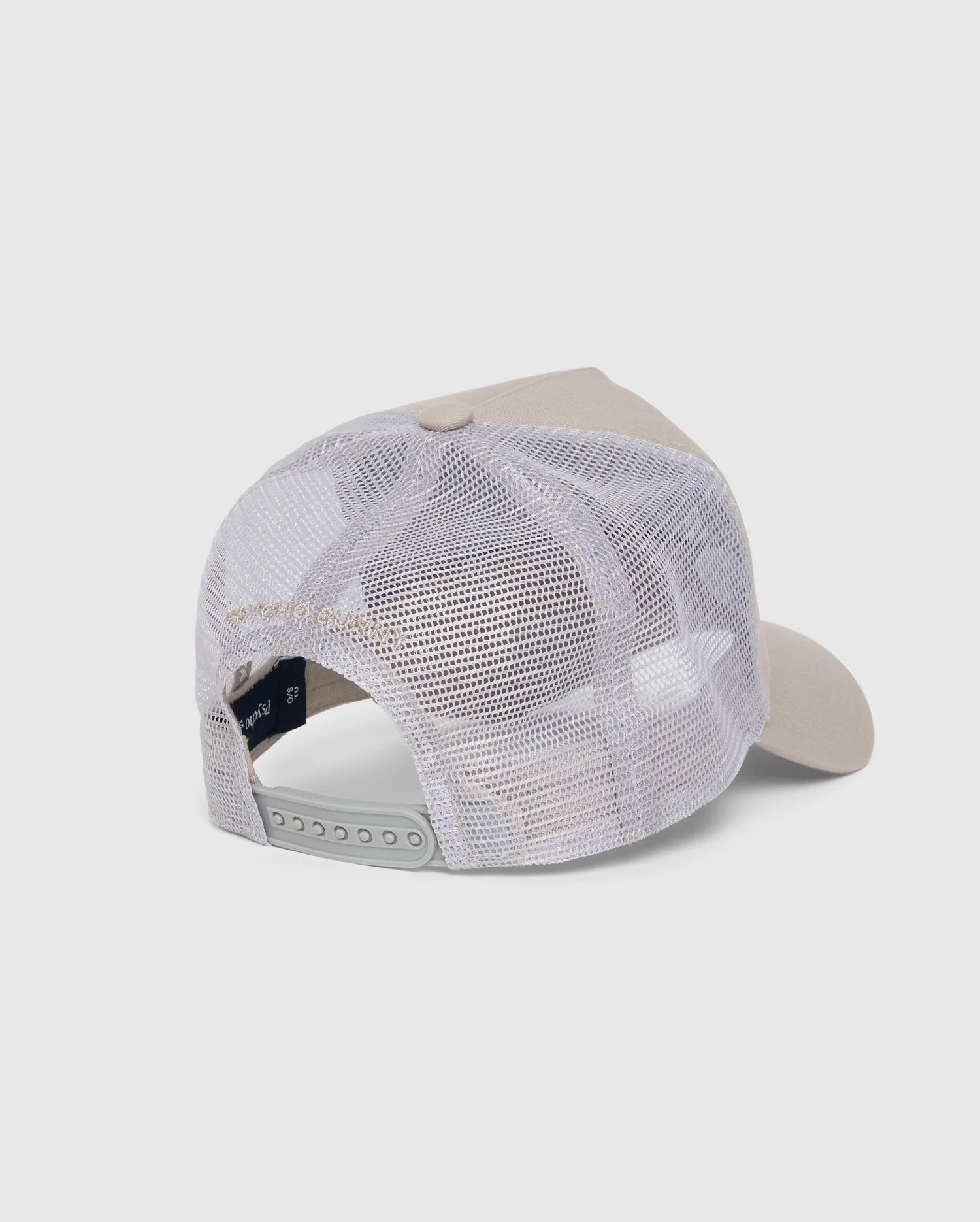 The back view of the KIDS MALTON TRUCKER CAP - B0A797D200 by Psycho Bunny showcases a beige and white design with a curved brim. The cap features a white mesh back for optimal ventilation and an adjustable snapback closure. Its front panel is solid and structured, made from cotton. The background is plain white.