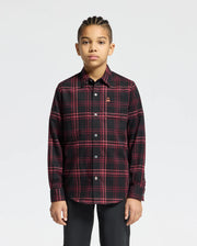 A person with braided hair wears a Psycho Bunny Kids Hayes Plaid Shirt - B0C842D200, showcasing black and red long sleeves, paired with black pants and standing against a plain white background.