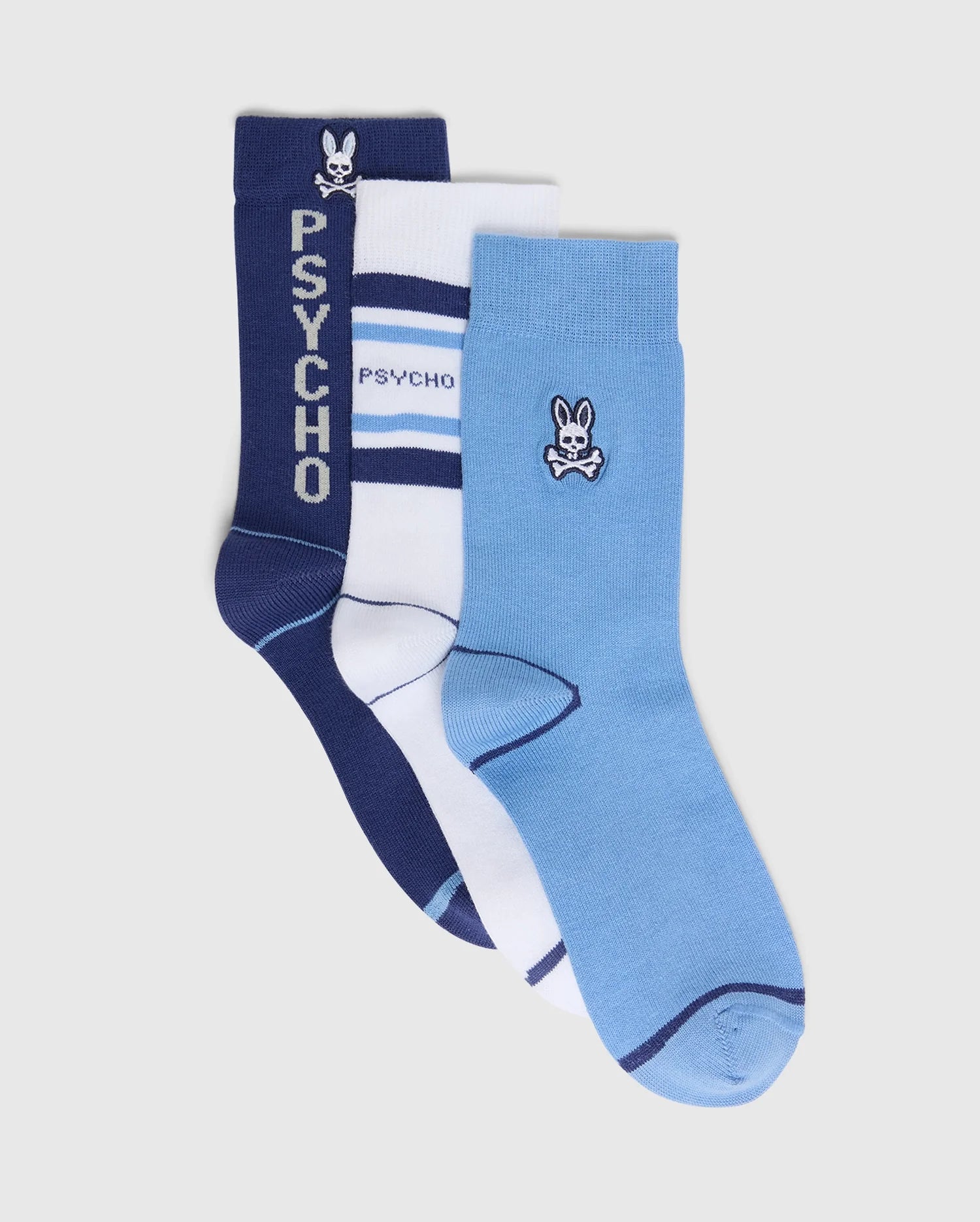 The KIDS 3 PACK FASHION DRESS SOCK - B0F504F200 by Psycho Bunny includes three Pima cotton pairs: navy with "Psycho" text and a bunny logo, white with navy stripes and "Psycho" text, and light blue with bunny logos, each offering unique designs and accents.