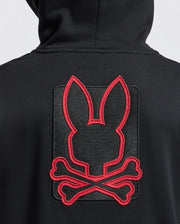A person wearing the KIDS PIERCE ESSENTIAL FRENCH TERRY ZIP HOODIE by Psycho Bunny, which showcases a large red outline of a bunny head above crossed bones on the back. The unique emblem merges elements of a skull and crossbones with bunny ears, bringing an unexpected twist to this classic style.