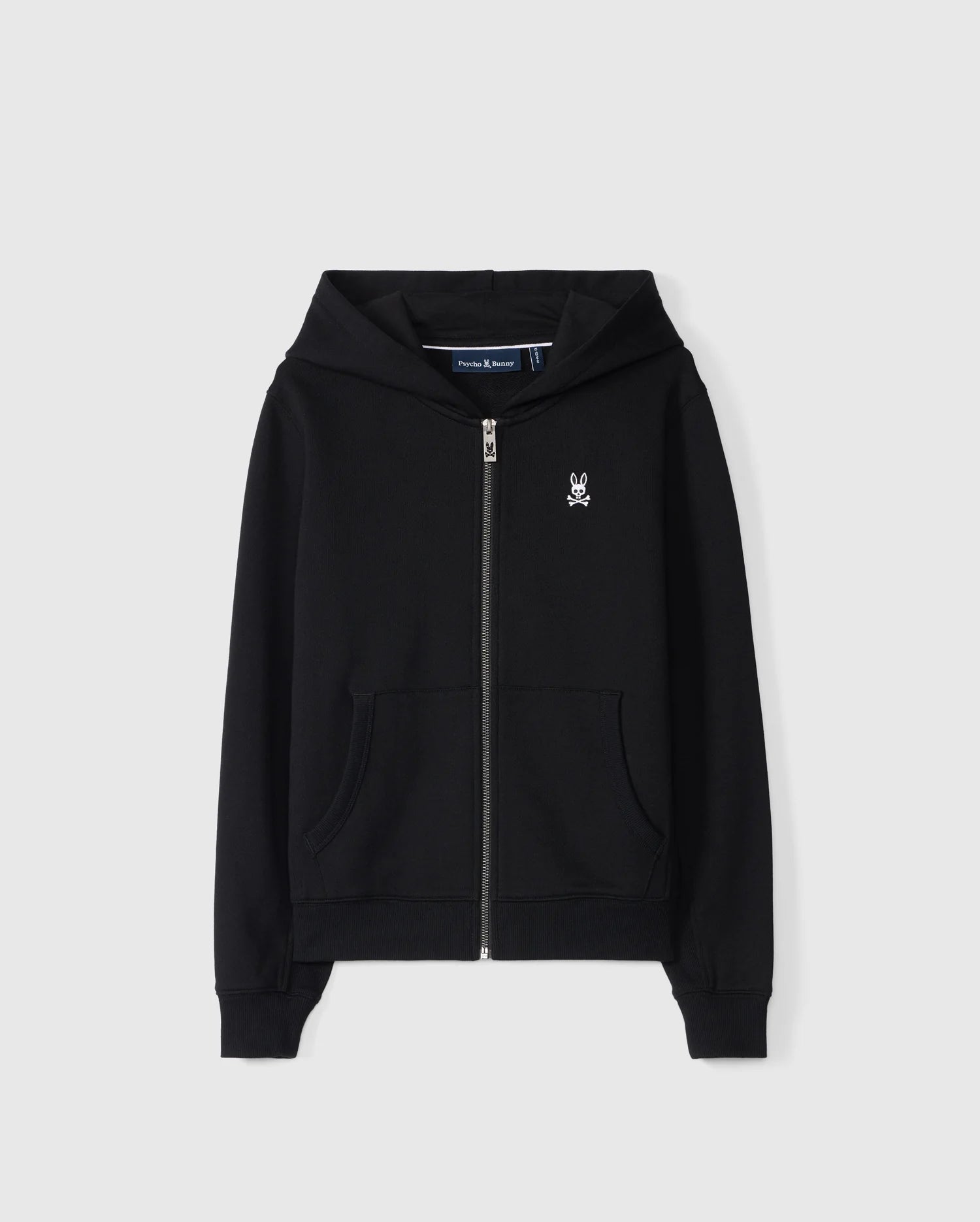 The KIDS LEVY ZIP FLEECE HOODIE - B0H720D200 by Psycho Bunny is a black French terry hoodie made from 100% cotton. It features a small white embroidered skull logo on the left chest, along with a front zipper and two pockets. The garment is showcased against a plain white background.