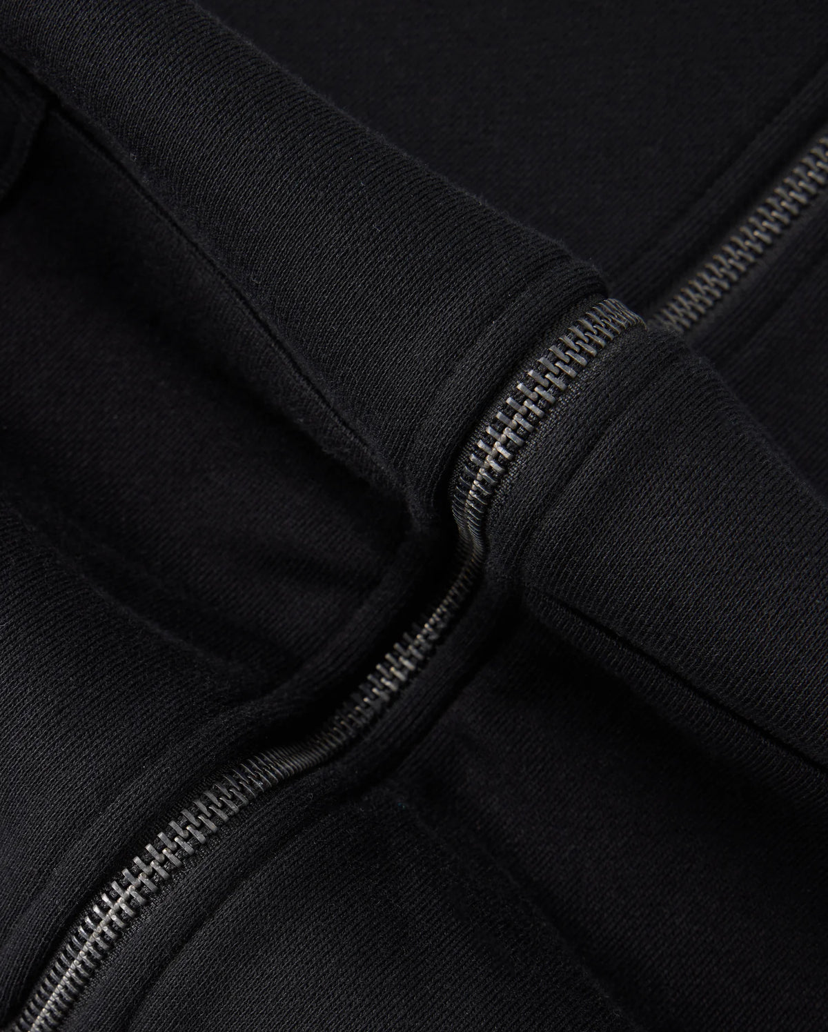 Close-up of a black 100% cotton fabric with two parallel zippers. The fabric, likely from the Psycho Bunny KIDS LEVY ZIP FLEECE HOODIE - B0H720D200, appears thick and durable. The metallic zippers interlock snugly, their shine contrasting subtly with the rich texture of the material.
