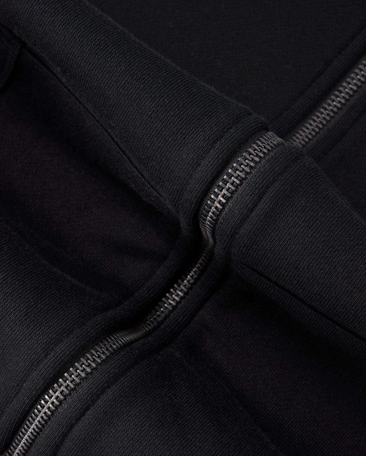 Close-up of a black 100% cotton fabric with two parallel zippers. The fabric, likely from the Psycho Bunny KIDS LEVY ZIP FLEECE HOODIE - B0H720D200, appears thick and durable. The metallic zippers interlock snugly, their shine contrasting subtly with the rich texture of the material.