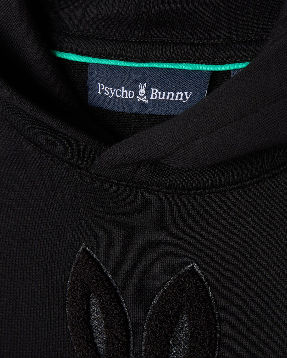 Close-up of the KIDS PACIFIC CHENILLE HOODIE - B0H930D200 in black, featuring a Psycho Bunny label at the collar. The French terry fabric showcases chenille embroidery in matching black, resembling bunny ears.