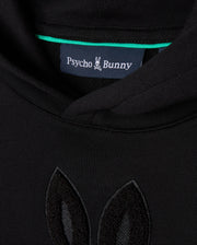 Close-up of the KIDS PACIFIC CHENILLE HOODIE - B0H930D200 in black, featuring a Psycho Bunny label at the collar. The French terry fabric showcases chenille embroidery in matching black, resembling bunny ears.