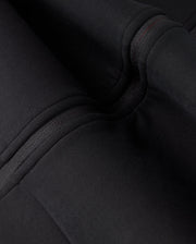 Close-up view of black fabric with detailed stitching and folds on the high-quality cotton-blend KIDS TRAVIS TRACK JACKET - B0J142D200 by Psycho Bunny. The texture and seams of the fabric are clearly visible.