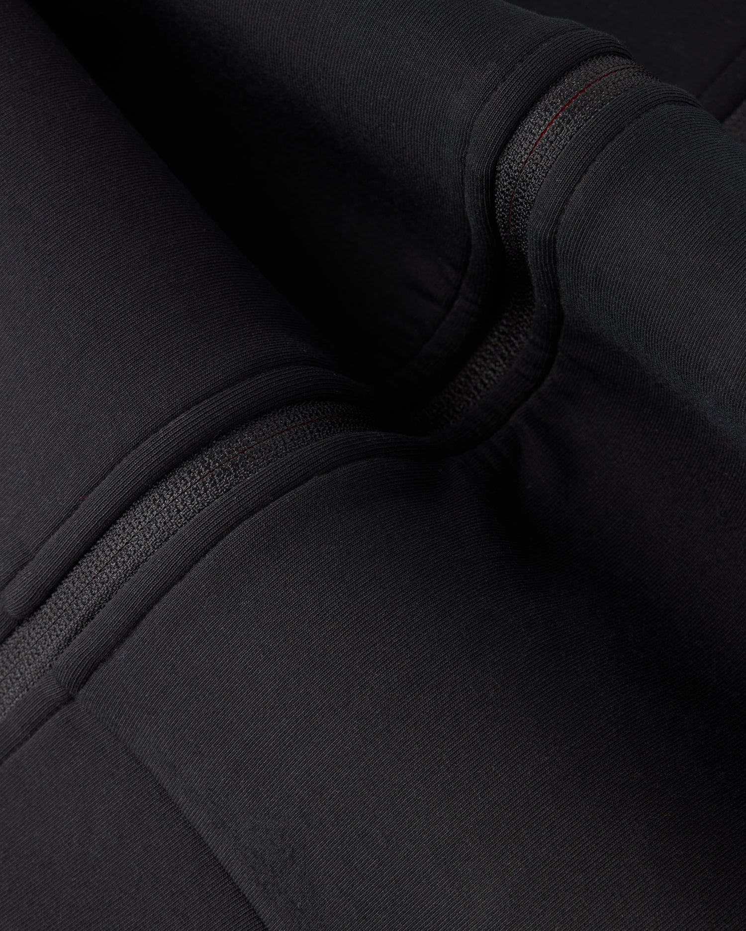Close-up view of black fabric with detailed stitching and folds on the high-quality cotton-blend KIDS TRAVIS TRACK JACKET - B0J142D200 by Psycho Bunny. The texture and seams of the fabric are clearly visible.