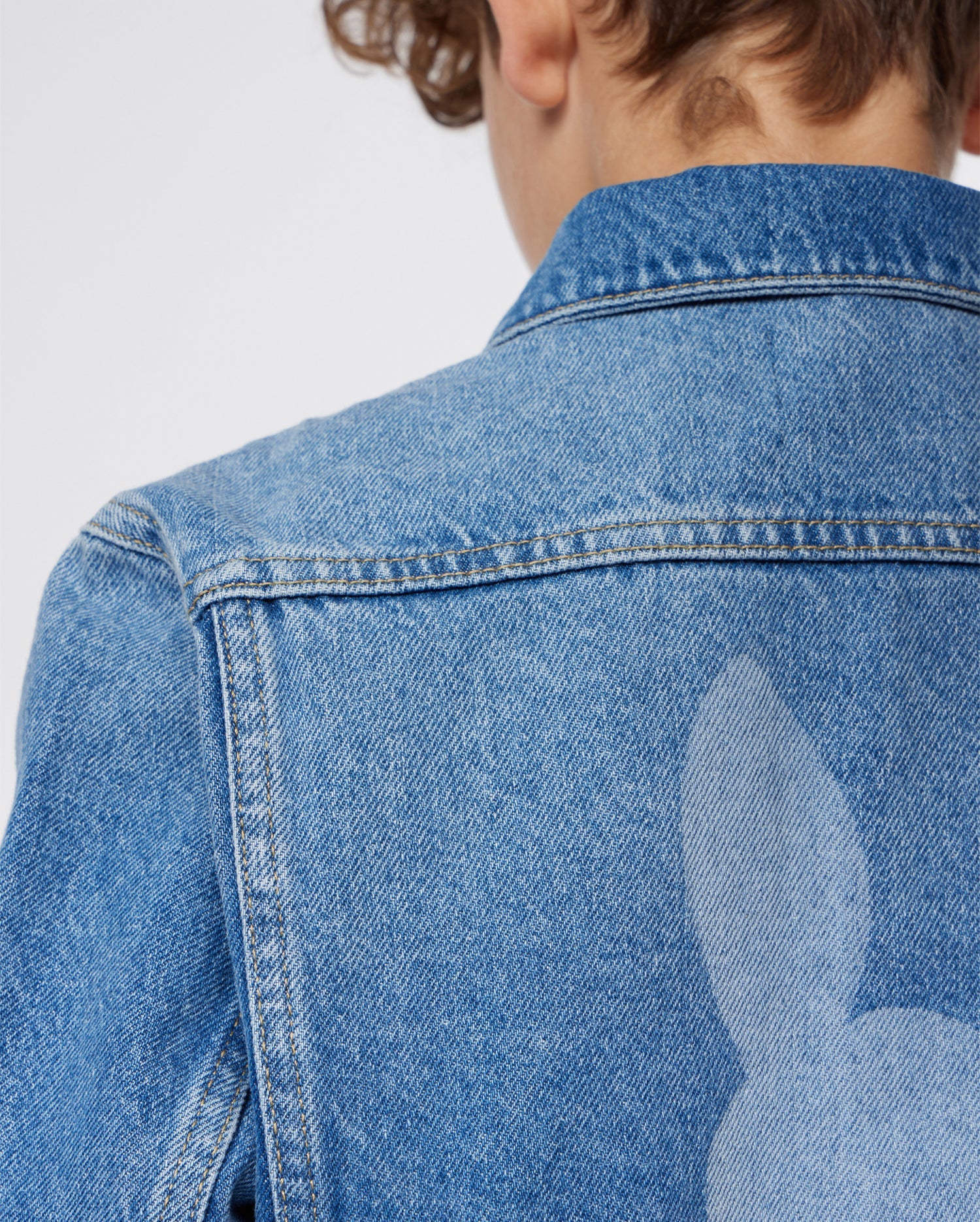 The back of a person wearing a KIDS PATHE DENIM JACKET - B0J741X1CO by Psycho Bunny made from upcycled cotton.