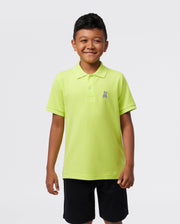 A smiling child, confident against a plain background, wears the Psycho Bunny KIDS CLASSIC POLO - B0K001CRPC in bright green. The regular fit Pima cotton piqué features a small emblem on the left side, enhancing their cheerful appearance.