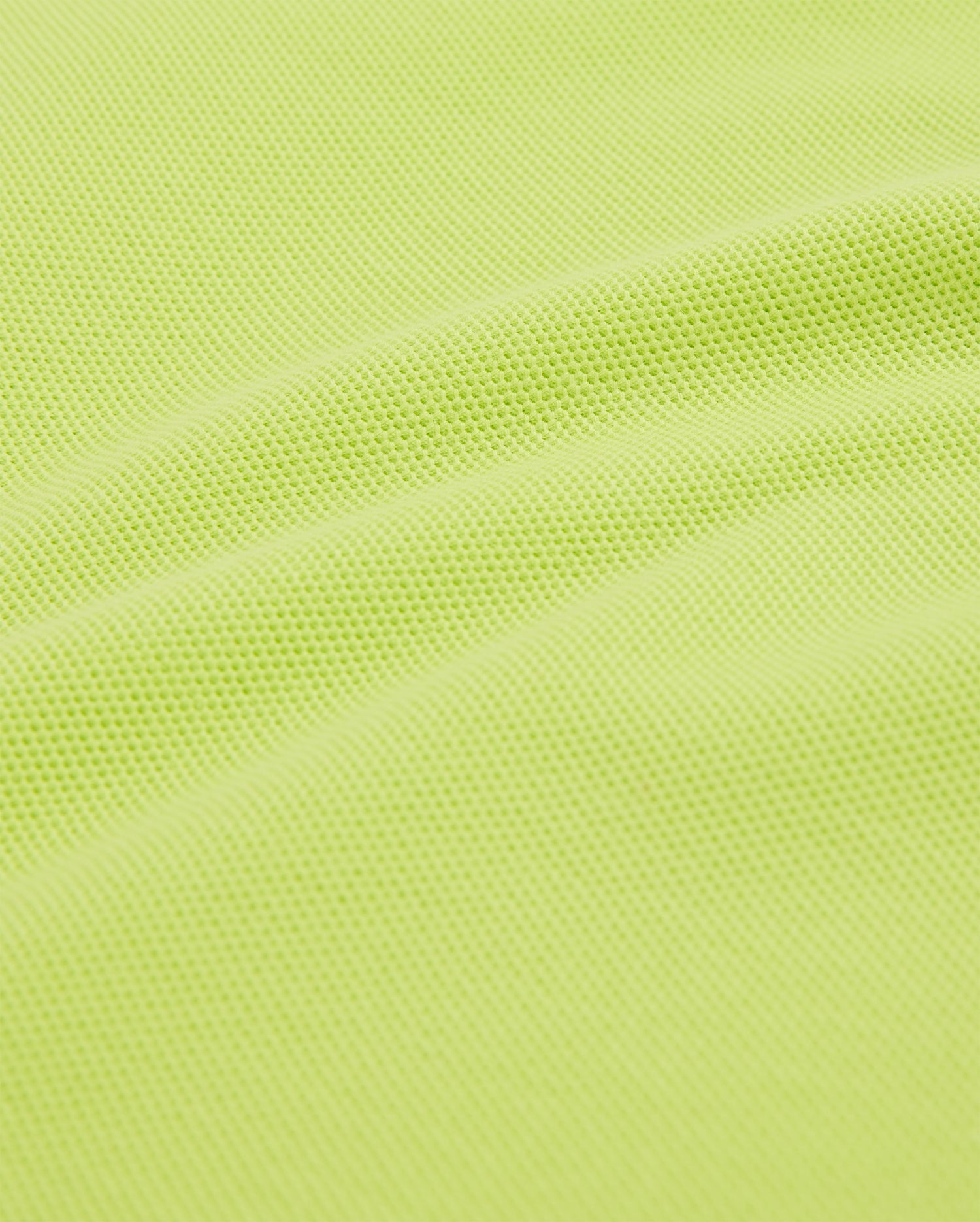 A close-up of the KIDS CLASSIC POLO - B0K001CRPC by Psycho Bunny shows a textured, lime green fabric with a subtle wave pattern, resembling classic piqué designs. Crafted from a breathable, slightly elastic mesh material like soft Pima cotton.