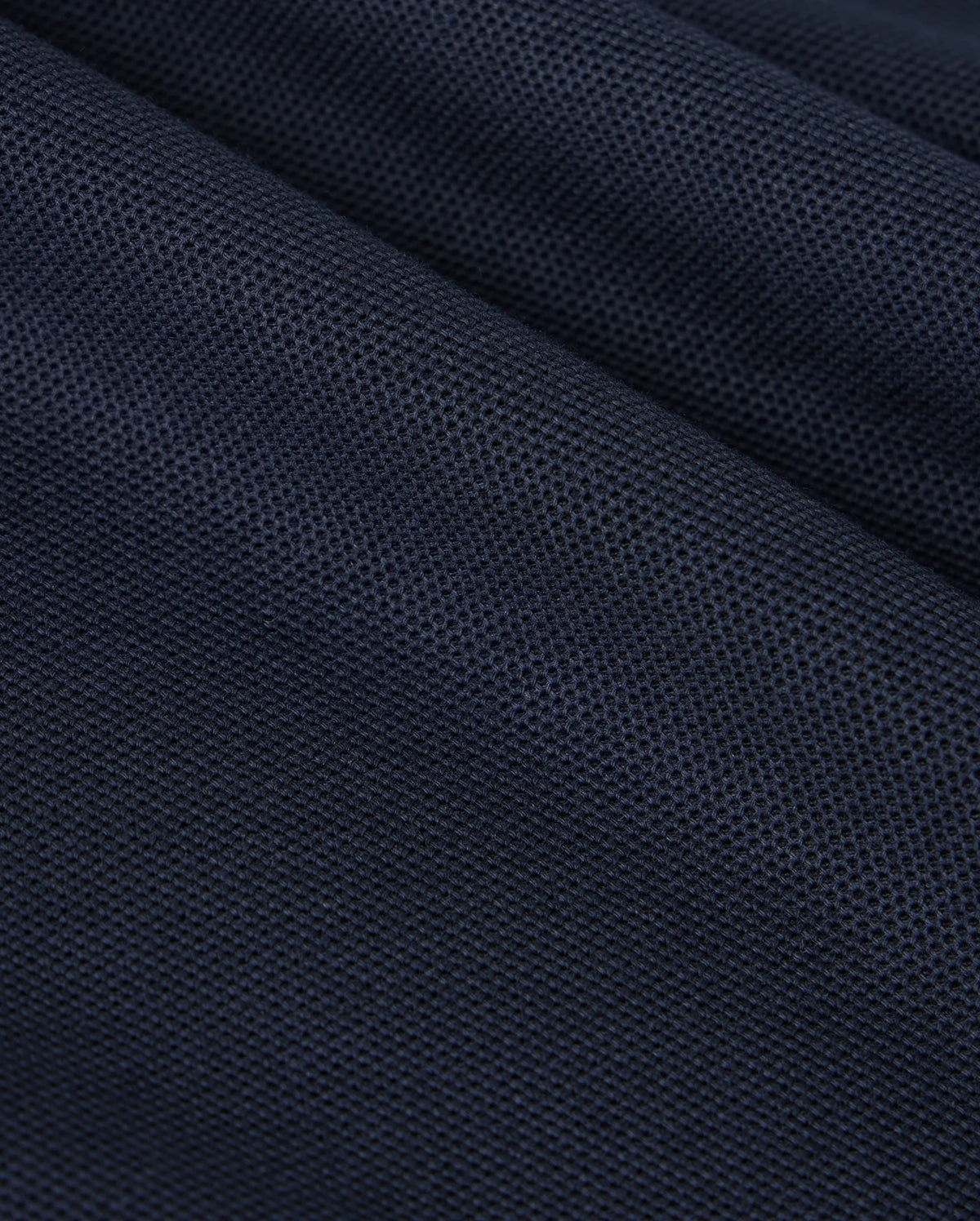 A close-up of a dark blue textured fabric reveals the fine woven pattern and small perforations characteristic of Pima cotton, similar to what's found in a Psycho Bunny KIDS CLASSIC PIQUE POLO SHIRT - B0K021AR00. The slightly folded material creates subtle shadows and highlights across its surface, reminiscent of a classic polo.