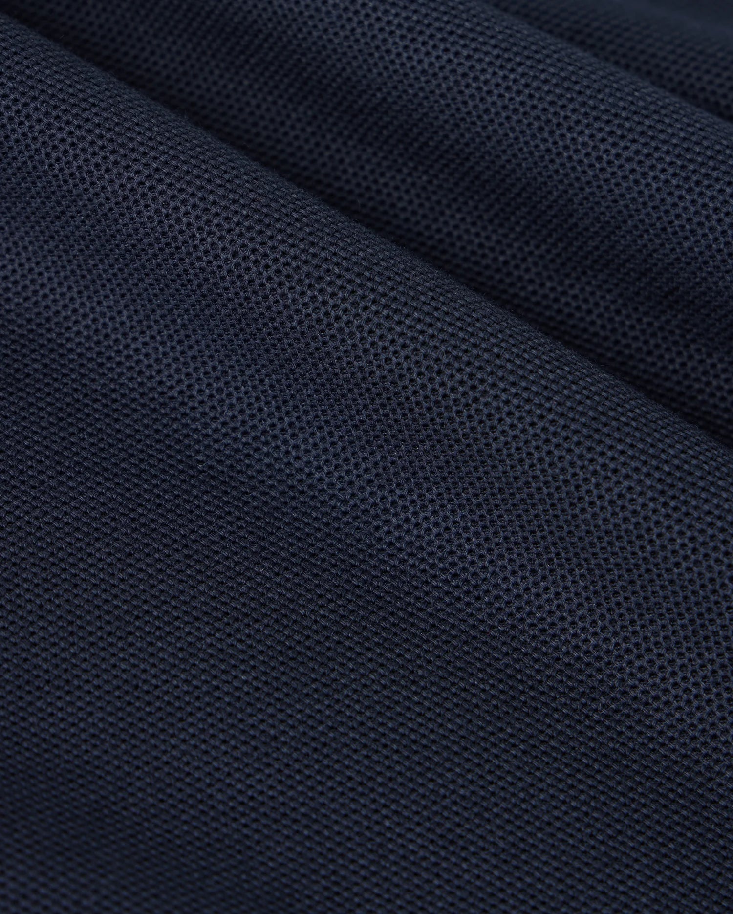 A close-up of a dark blue textured fabric reveals the fine woven pattern and small perforations characteristic of Pima cotton, similar to what's found in a Psycho Bunny KIDS CLASSIC PIQUE POLO SHIRT - B0K021AR00. The slightly folded material creates subtle shadows and highlights across its surface, reminiscent of a classic polo.