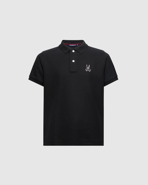 Introducing the KIDS ALEXANDER PIQUE POLO - B0K101E200 from Psycho Bunny. This fashionable black polo for kids features short sleeves and a buttoned collar, adorned with an embroidered logo showcasing a cartoon rabbit with crossed bones on the chest, elegantly set against a light gray background.