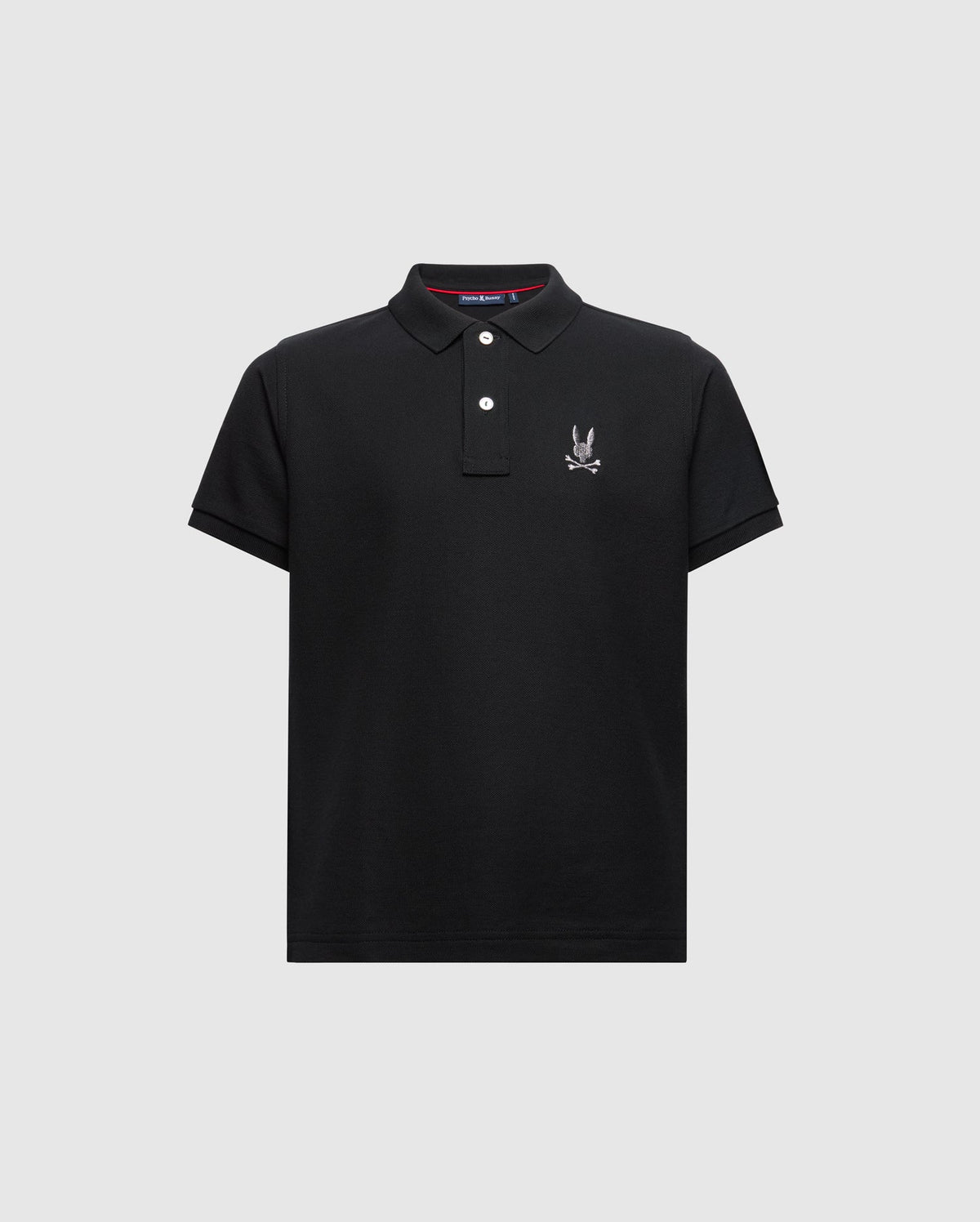 Introducing the KIDS ALEXANDER PIQUE POLO - B0K101E200 from Psycho Bunny. This fashionable black polo for kids features short sleeves and a buttoned collar, adorned with an embroidered logo showcasing a cartoon rabbit with crossed bones on the chest, elegantly set against a light gray background.