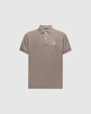 The KIDS ALEXANDER PIQUE POLO - B0K101E200 by Psycho Bunny is a chic children's polo shirt in a gentle beige color, made from high-quality Pima cotton. It includes a traditional collar and short sleeves, adorned with an understated embroidered palm tree logo on the left chest. Presented against a simple light grey background for a sophisticated appeal.