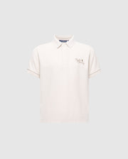 The KIDS DESERT PIQUE POLO from Psycho Bunny in cream offers timeless style with a collar, short sleeves, and subtle left chest embroidery of text and a logo. Crafted from luxurious Pima cotton, its light gray background adds to its classic elegance.