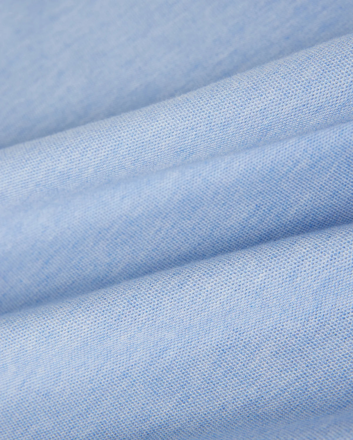 Close-up of soft, folded blue fabric with a smooth and slightly textured surface. The fabric's weave is visible, highlighting its fine, uniform texture. Made from luxurious Pima cotton polo material used in the KIDS WINDCREST PIQUE POLO SHIRT - B0K592C200 by Psycho Bunny, the appearance is clean and gentle, creating a sense of comfort and coziness.