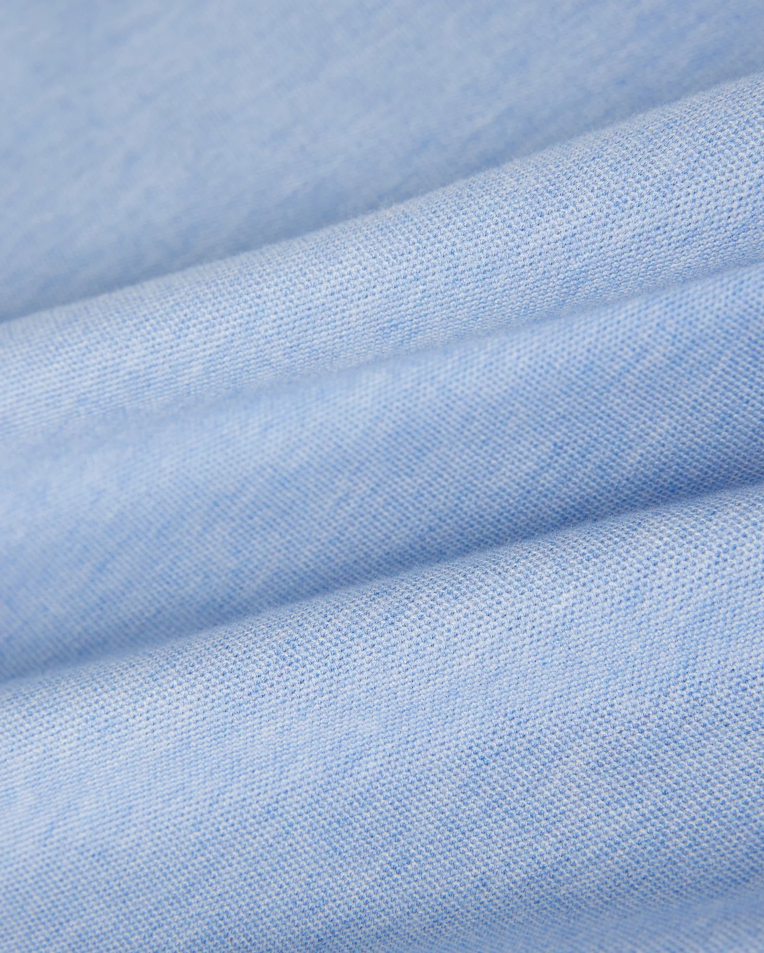 Close-up of soft, folded blue fabric with a smooth and slightly textured surface. The fabric's weave is visible, highlighting its fine, uniform texture. Made from luxurious Pima cotton polo material used in the KIDS WINDCREST PIQUE POLO SHIRT - B0K592C200 by Psycho Bunny, the appearance is clean and gentle, creating a sense of comfort and coziness.