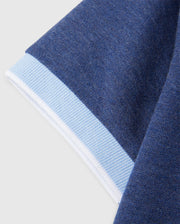 Close-up of a garment sleeve featuring a dark blue knit fabric with a light blue and white cuff. The texture of the Psycho Bunny KIDS WINDCREST PIQUE POLO SHIRT - B0K592C200 fabric is clearly visible, highlighting the differences between the main sleeve material and the smooth, ribbed cuff.