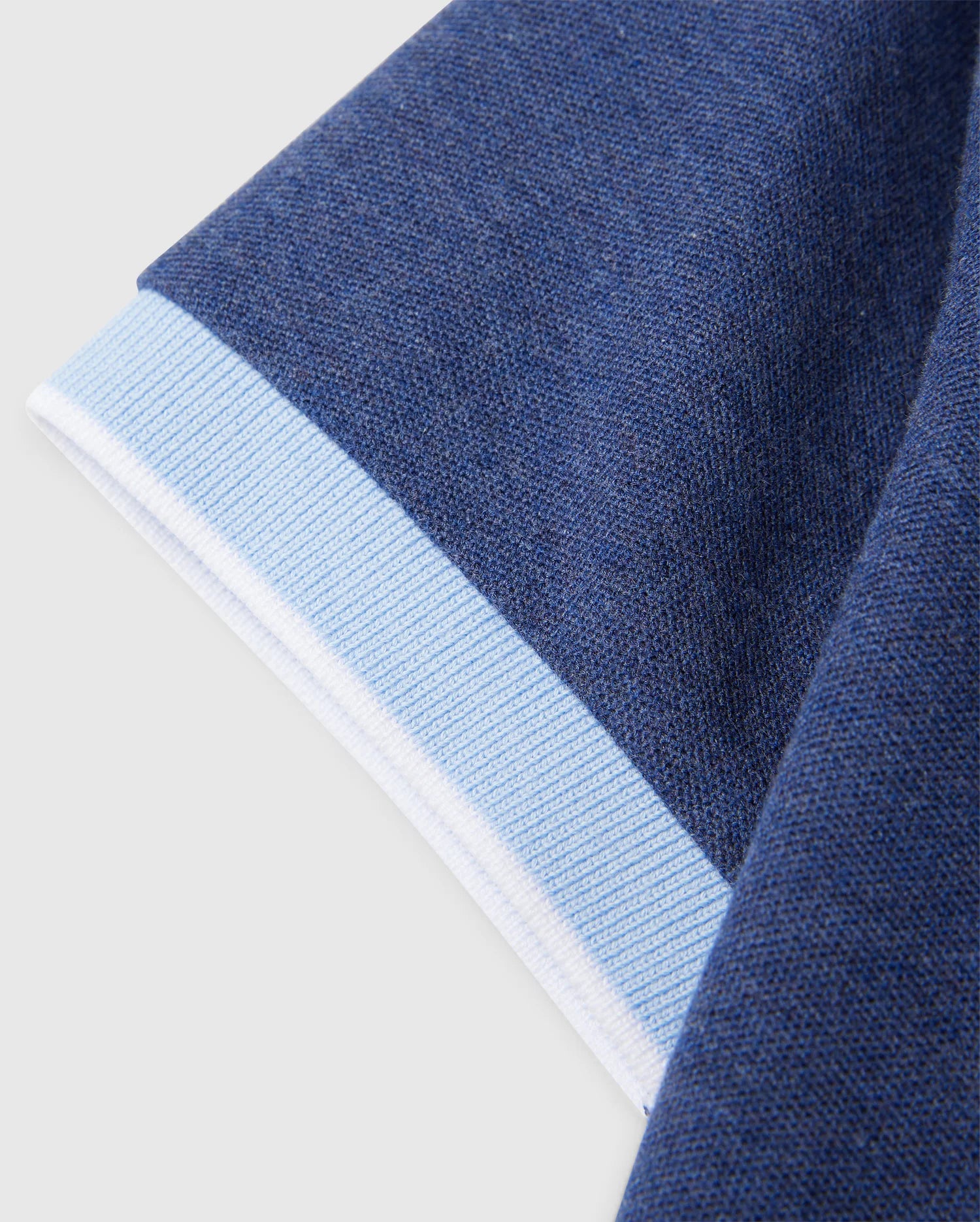 Close-up of a garment sleeve featuring a dark blue knit fabric with a light blue and white cuff. The texture of the Psycho Bunny KIDS WINDCREST PIQUE POLO SHIRT - B0K592C200 fabric is clearly visible, highlighting the differences between the main sleeve material and the smooth, ribbed cuff.