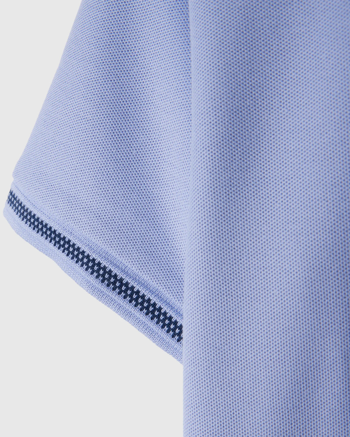 Close-up of a textured light blue fabric, possibly the sleeve of the Psycho Bunny Kids Riviera Pique Polo Shirt (B0K640C200), featuring a black and white striped trim along the edge.