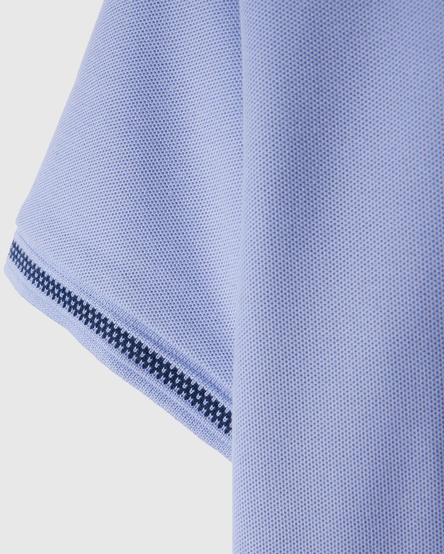 Close-up of a textured light blue fabric, possibly the sleeve of the Psycho Bunny Kids Riviera Pique Polo Shirt (B0K640C200), featuring a black and white striped trim along the edge.