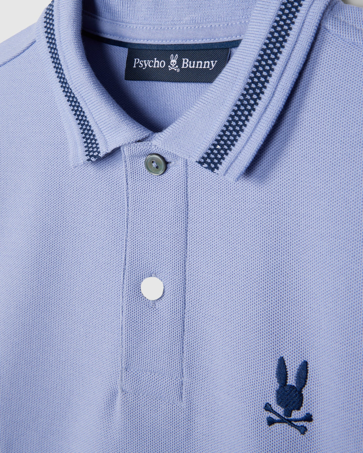 A close-up of the KIDS RIVIERA PIQUE POLO SHIRT - B0K640C200 by Psycho Bunny in light blue Pima cotton piqué showcases a dark blue embroidered chest Bunny logo with a bunny and crossbones. The collar features a striped pattern, and the shirt comes with two buttons.