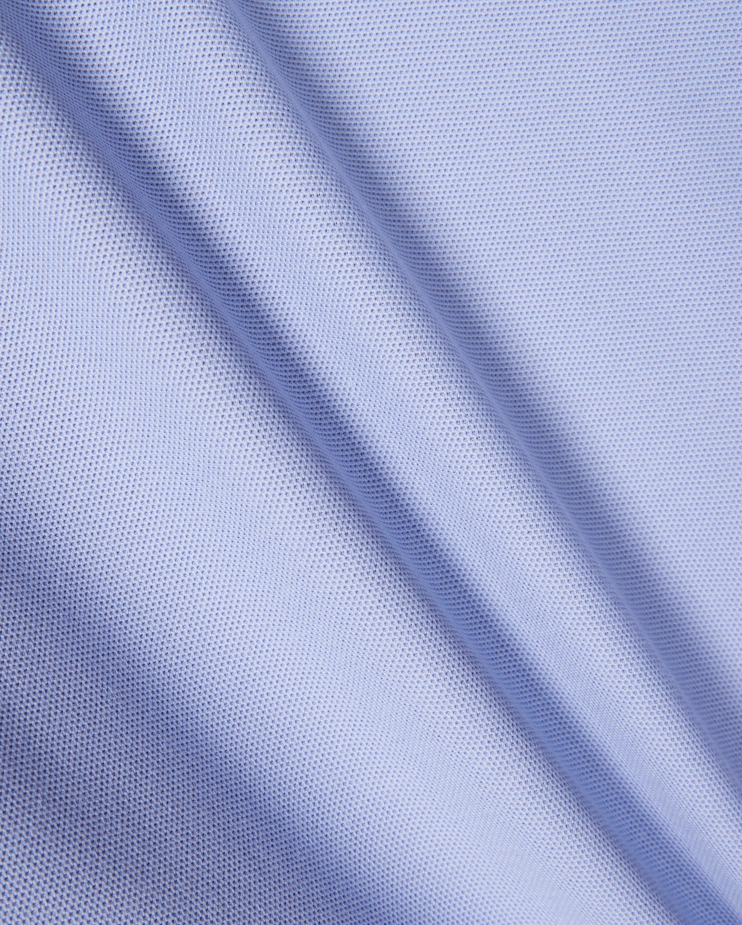 Close-up of light blue textured fabric with a fine mesh pattern, similar to Pima cotton piqué. The material shows gentle diagonal folds, indicative of its soft drape and smooth surface, echoing the refined elegance characteristic of the Psycho Bunny KIDS RIVIERA PIQUE POLO SHIRT - B0K640C200.