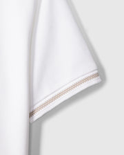 Close-up of the sleeve of a Kids Riviera Pique Polo Shirt - B0K640C200 by Psycho Bunny, made from textured Pima cotton fabric. The hem of the sleeve features two rows of intricate beige stitching, adding a decorative element to the minimalist design. The background is plain and neutral, ensuring the focus remains on the sleeve.