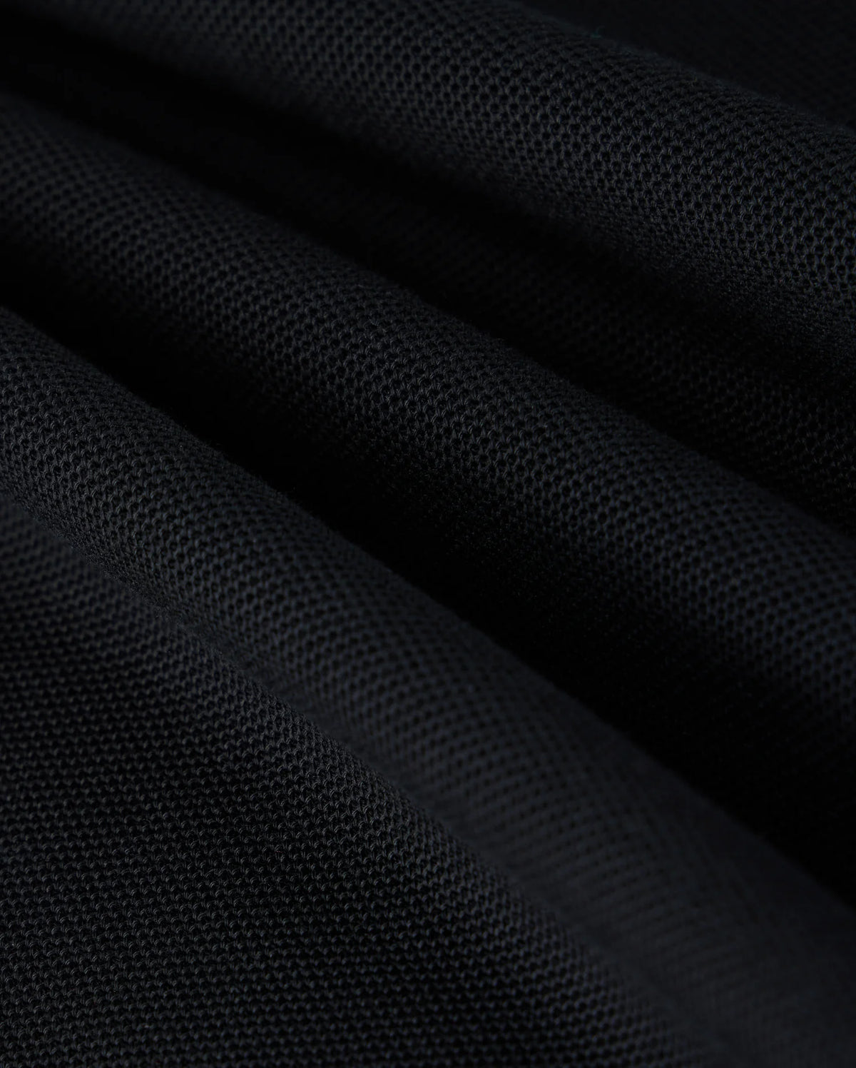 Close-up image of black Pima cotton piqué fabric with a textured surface, showcasing the intricate weave pattern. The fabric is arranged in folds, creating a play of light and shadow across its surface, reminiscent of the sophisticated elegance found in Psycho Bunny's KIDS KAYDEN PIQUE POLO - B0K675C200.