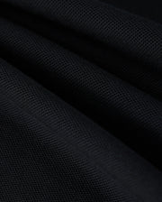 Close-up image of black Pima cotton piqué fabric with a textured surface, showcasing the intricate weave pattern. The fabric is arranged in folds, creating a play of light and shadow across its surface, reminiscent of the sophisticated elegance found in Psycho Bunny's KIDS KAYDEN PIQUE POLO - B0K675C200.