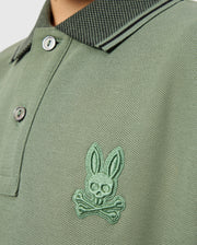 A detailed look at the KIDS MALTON PIQUE POLO SHIRT - B0K950D200 by Psycho Bunny, this green polo is made from soft pima cotton and showcases a skull-and-crossbones logo with rabbit ears on the chest. The design includes a patterned collar, diamond piqué-patterned cuffs, and two buttons for added style.
